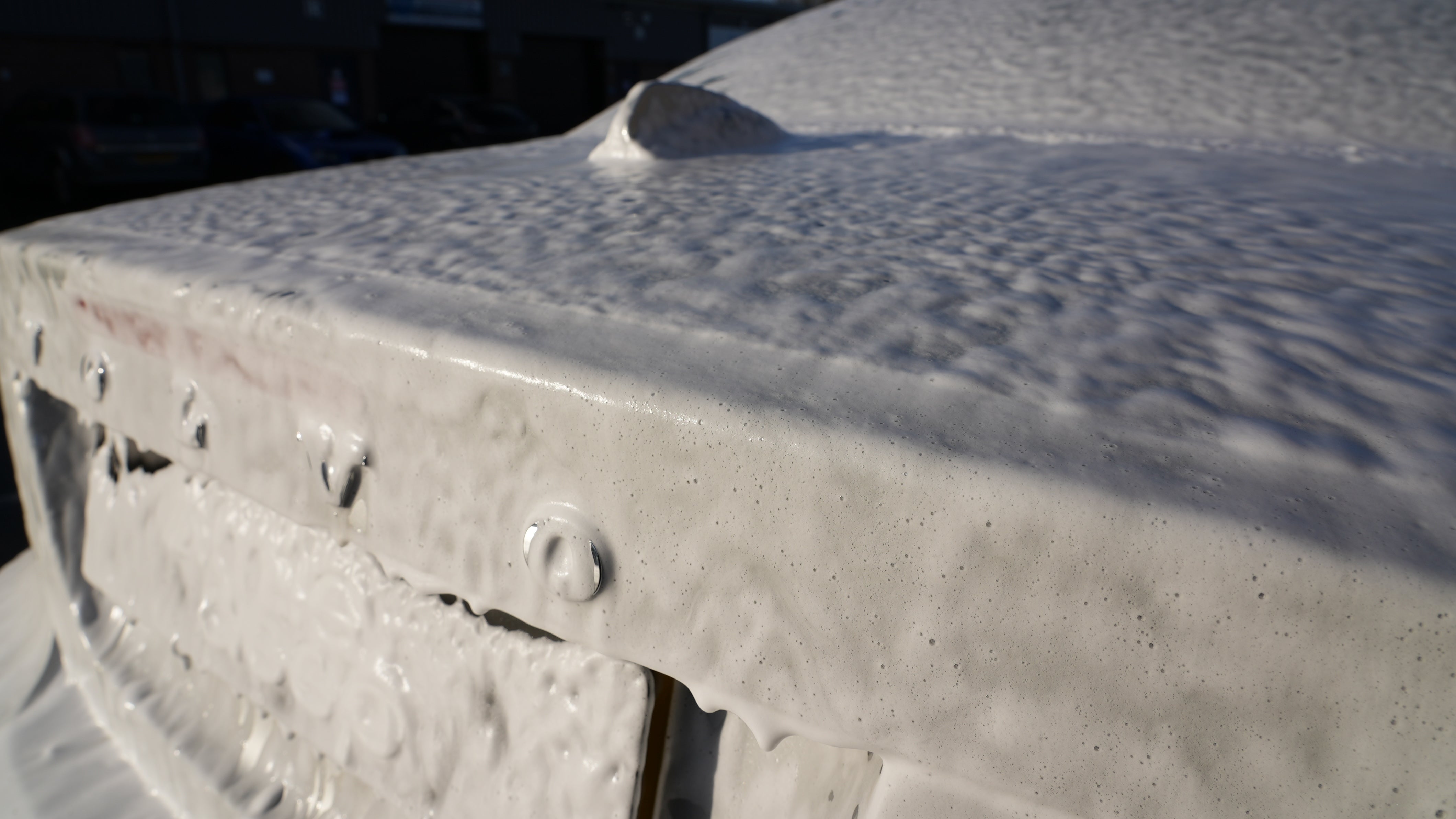 Close-up of thick white snow foam covering a car's boot and rear end during the pre-wash stage of professional car detailing.